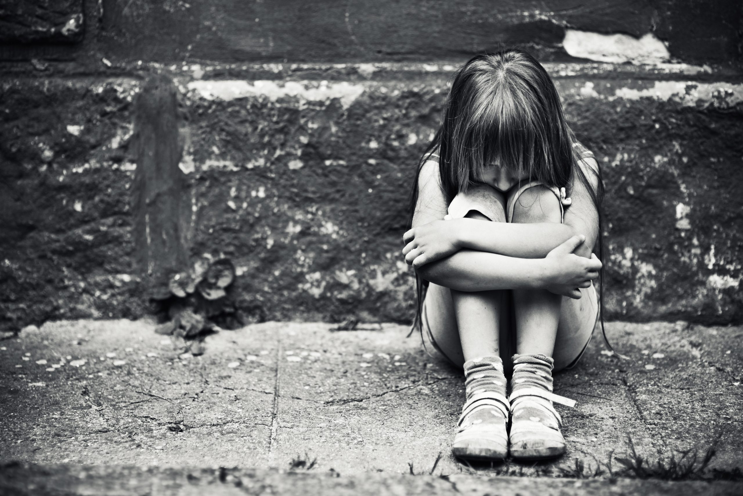 Depressed child sitting at weargered sidewalk. Fine noise applied.