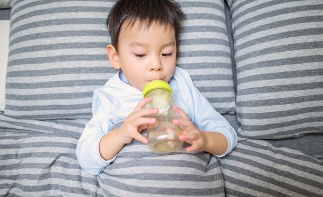toddler drinking from bottle on bed