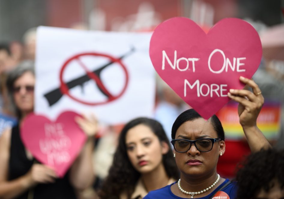 A Black woman wearing glasses and pearls holds a red heart above her head that reads