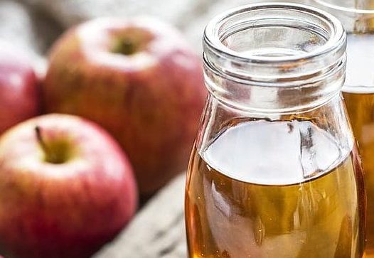 a glass jar filled with apple juice in the foreground with apples and other jars in the background