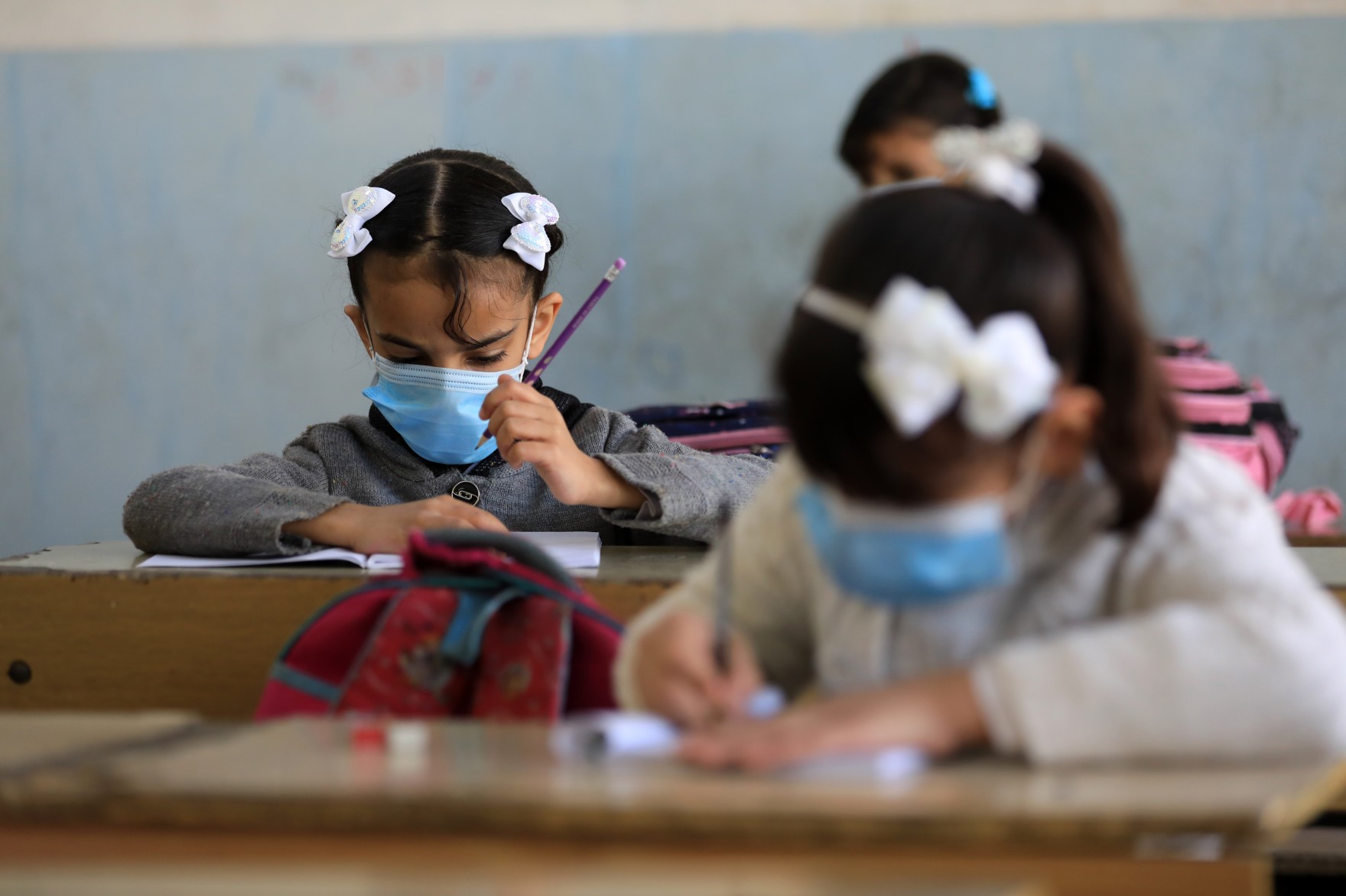girls sit at desks in classroom with masks