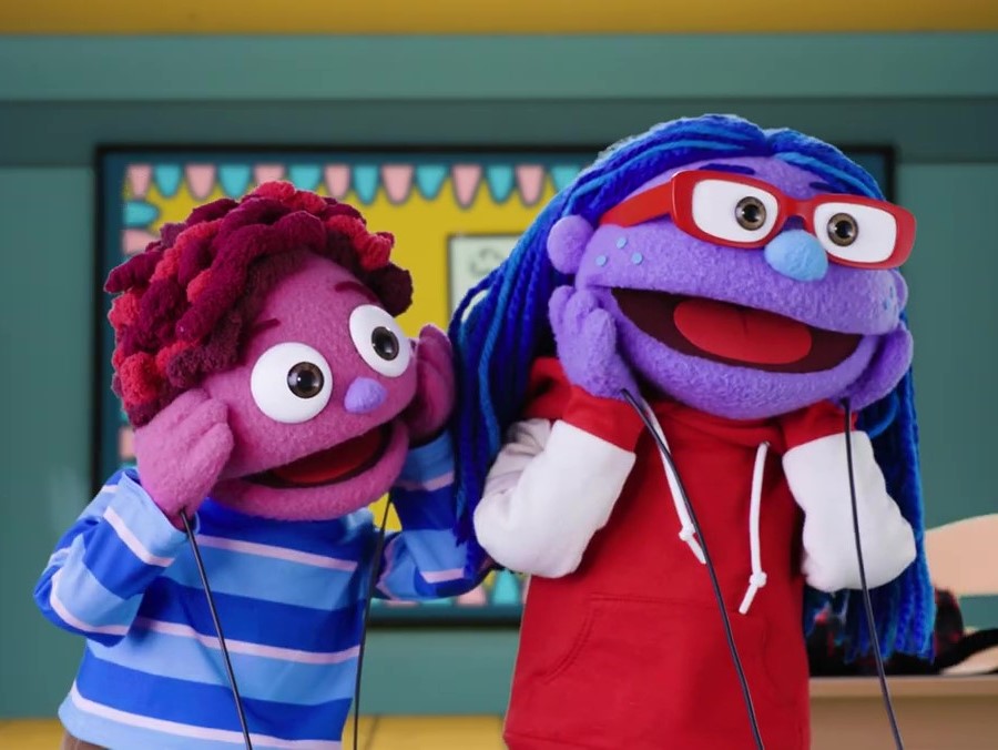 two puppets smile and hold their hands to their face