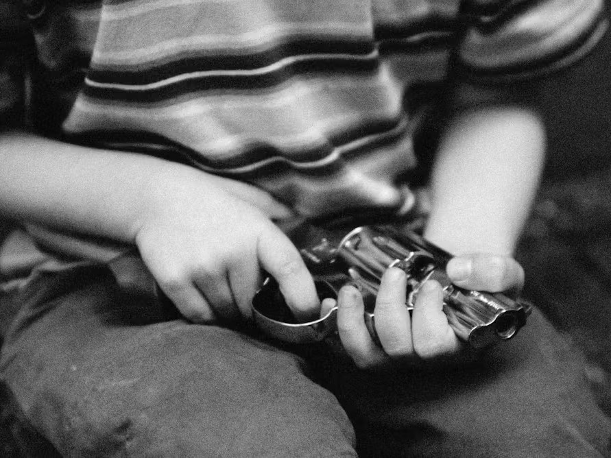 Child sitting with striped shirt and holding gun on their lap. Picture only shows bottom of torso and top of legs Laurent Hamels via Getty Images