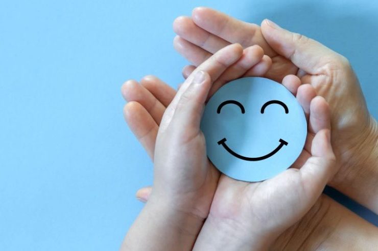 Two sets of white hands (adult and child) holding a cardboard smiley face.