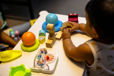 toddler playing with blocks and toys on white table. We see the child's back.