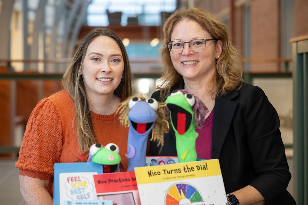 Emily Wicks and Sandy Chafouleas smile and hold three sock puppets and books from the Fell Your Best Self Toolkit